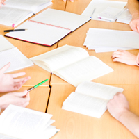 Mehrere Bücher liegen aufgeschlagen auf einem Tisch und einige Hände und Stifte sind sichtbar.